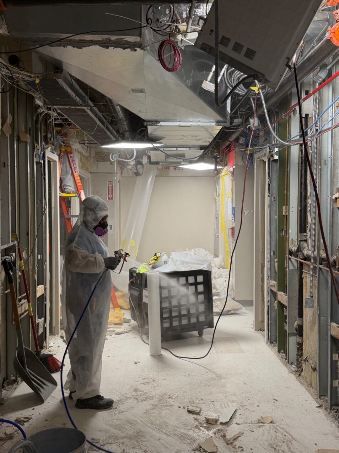 Worker in full PPE spraying in a gutted hallway